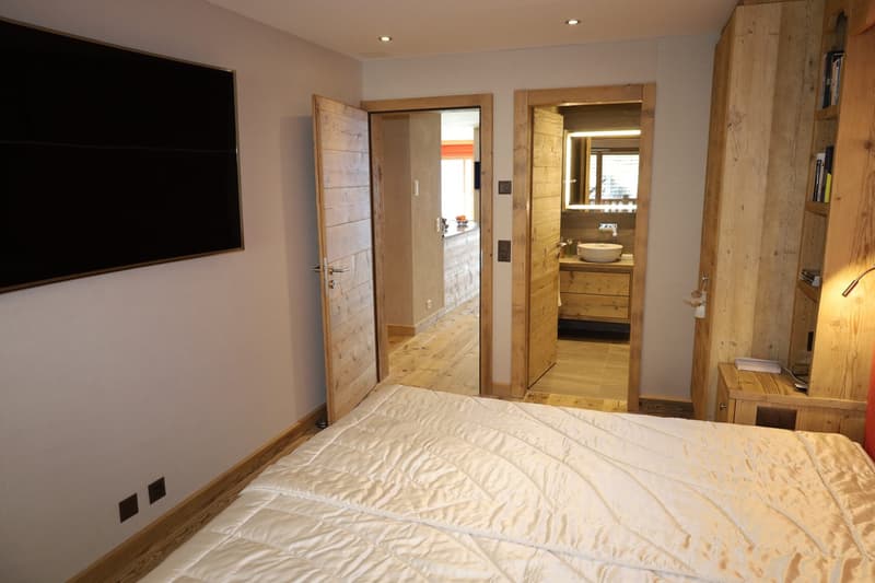 bedroom with bed, flat screen TV, wooden wardrobe, mirror, sink, two doors, one leading to bathroom