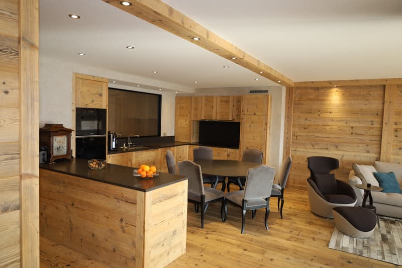 wooden interior, kitchen island with fruits, dining table with chairs, seating area with couch, coffee table, decorative lamp, kitchen area with sink, refrigerator, oven