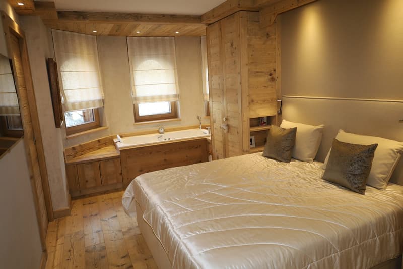 Large bedroom with wooden floor, large bed, wooden walls, bathroom with bathtub and windows