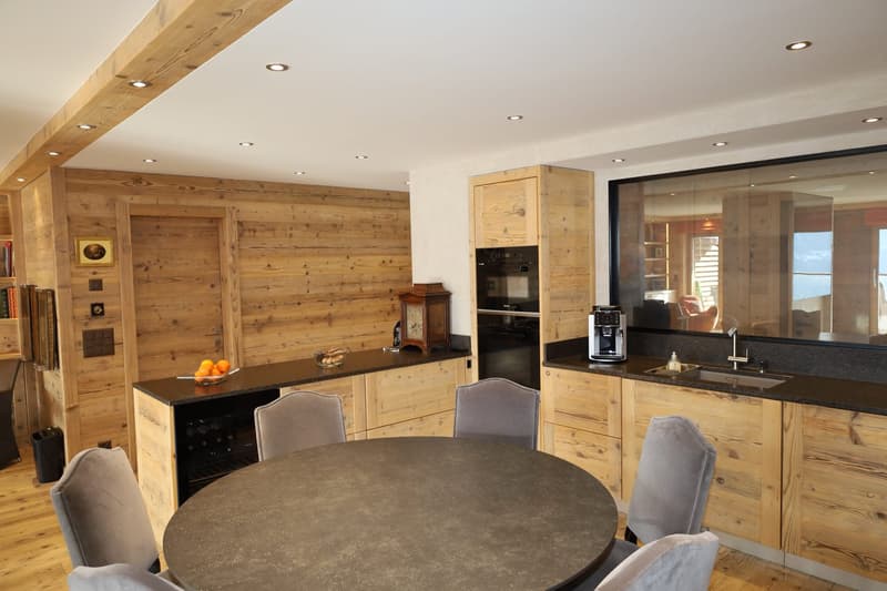 wooden walls, wooden floor, large table, grey chairs, wooden cabinets, sink, gas stove, oven, microwave, refrigerator