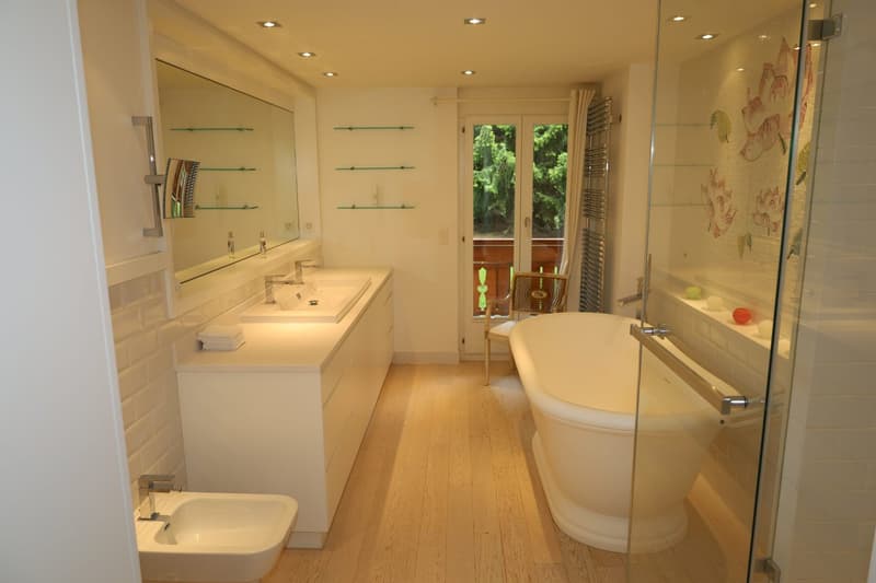 Bathtub, two sinks, mirror, wooden floor, glass shower, small chair, radiator, exit to balcony