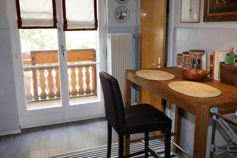 white radiator, wooden table, chair, table mats, basket, books, fruit bowl, door to balcony