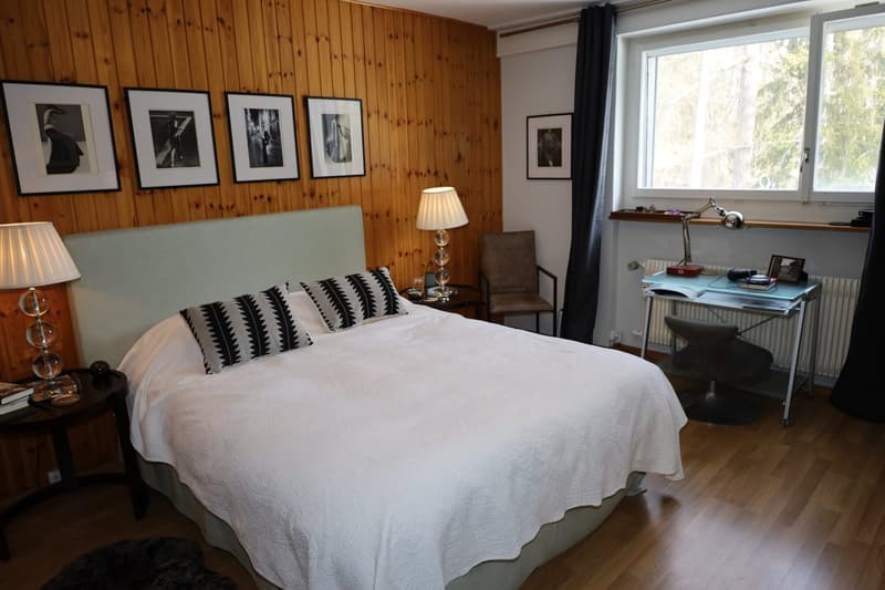 Bedroom with bed, 2 lamps, chair, desk, picture frames, radiator, window, black curtains