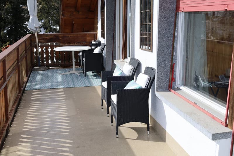 Balcony with wooden railings, wooden floor, chairs and table, rug, outdoor umbrella, view of surrounding area
