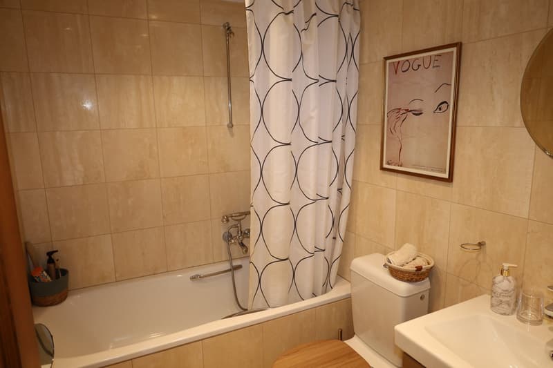 Bathroom with bathtub, shower, toilet, sink, mirror, a shelf, basket, soap dispenser and a wall-mounted basket with towels