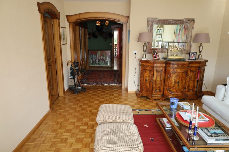 Wood floor, wooden door, hallway, two lamps, coffee table, sofa, rug, mirror, sideboard, picture frames