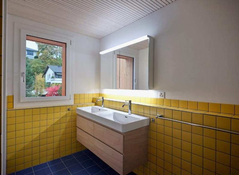 Modern bathroom with yellow tiles, double sink, large mirror, wooden cabinet, blue floor, natural light