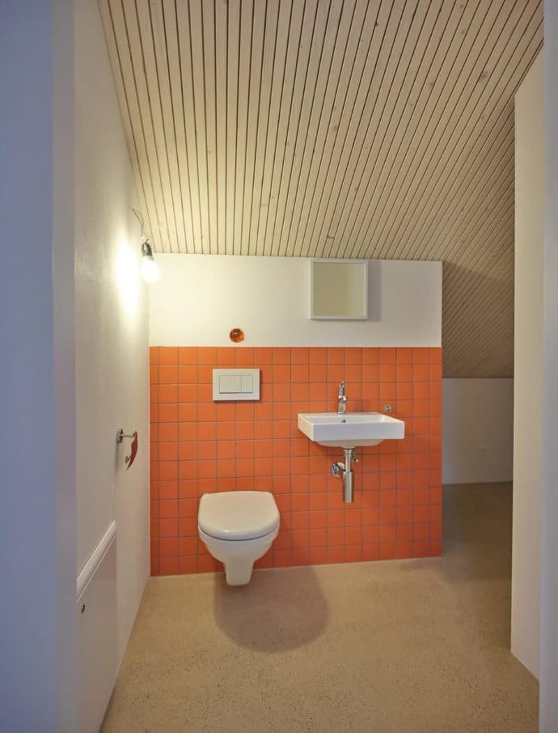 Compact bathroom with white toilet, white sink, and orange tiles