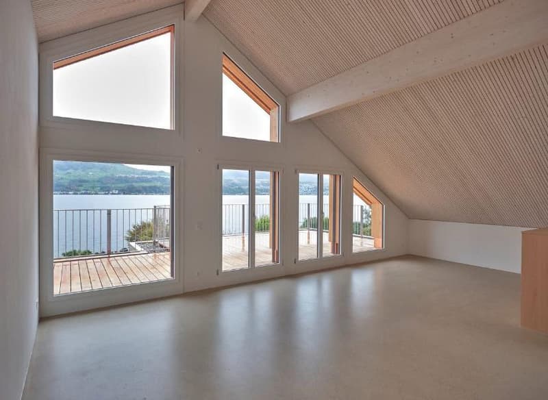 spacious attic room with large windows and sliding doors leading to balcony, wooden beams, hardwood flooring, stunning lake view