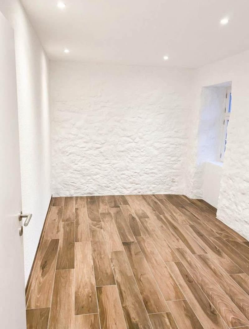 Empty room with wooden floors and white walls, window at the end of the room