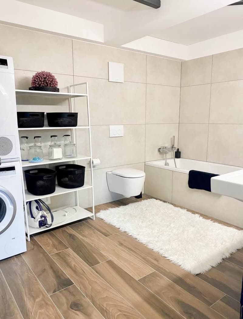 modern bathroom, wooden floor, tiled walls, white shelving, iron, storage baskets, white bathtub, sink, toilet
