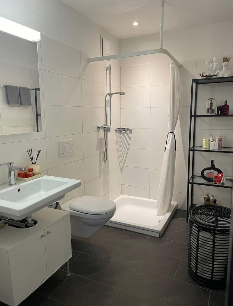 Small bathroom with a toilet, shower, and sink; all white tiles