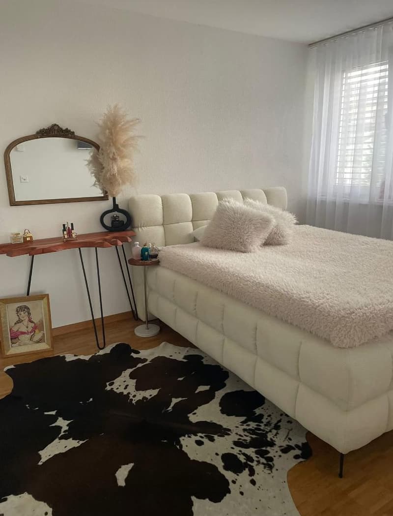 white upholstered bed with headboard, wooden side table, wooden console table, framed picture, mirror, cowhide rug, cowhide blanket, cushions
