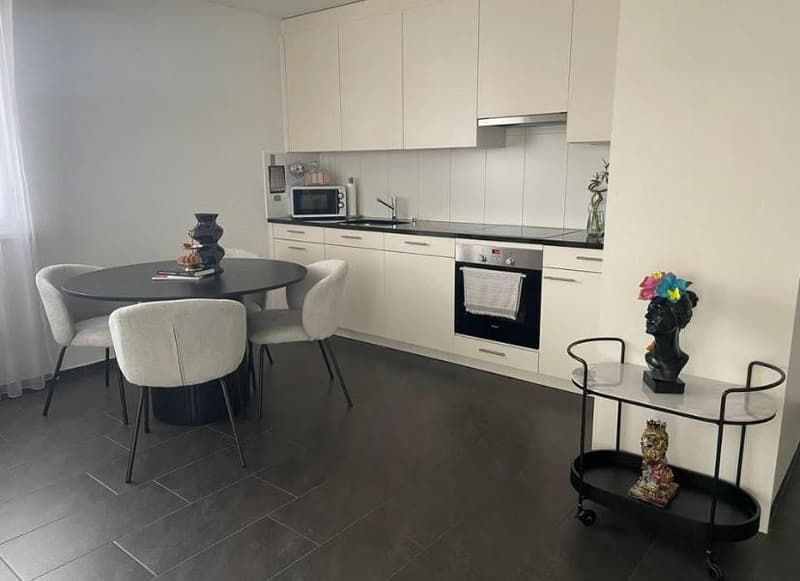 modern kitchen with dining area, white cabinets, black tiled floor, table with chairs, microwave, oven, stove, and decorative items