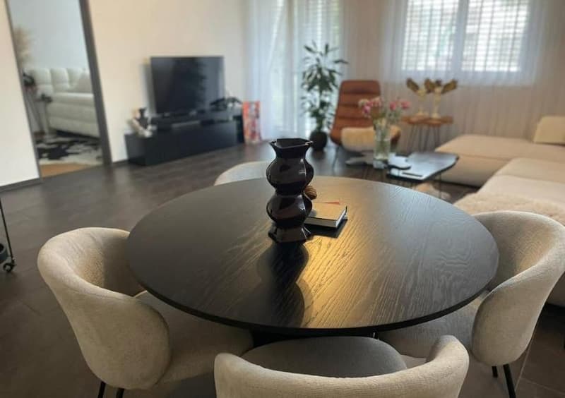 a living room with a round table, white chairs, a black tv, and potted plants