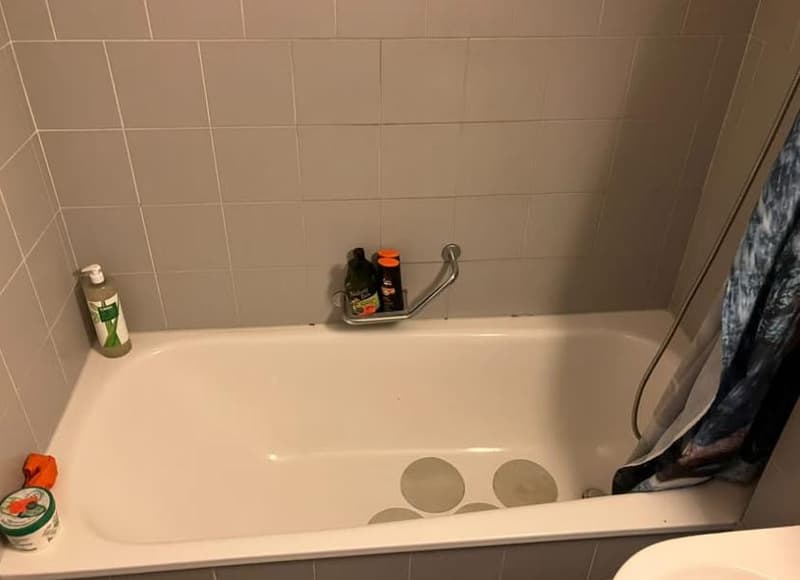 white bathtub, tiled walls, toiletries on the tub, shower curtain, white toilet