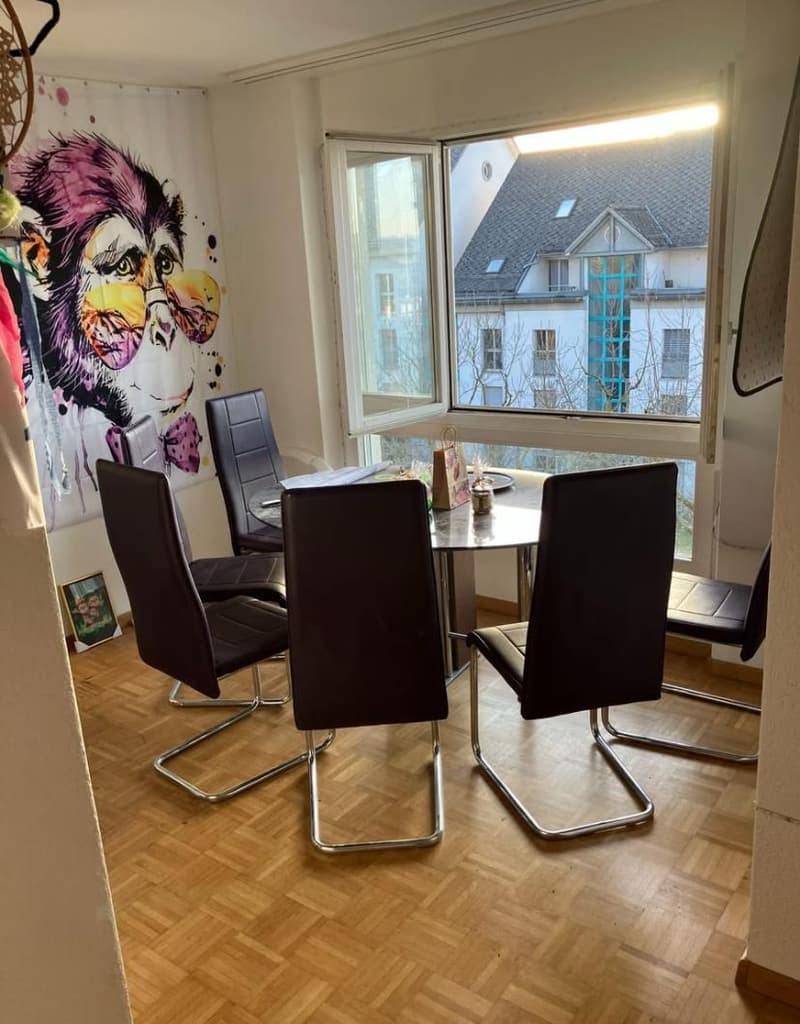 4 black dining chairs around a small round table, white walls, large window, wooden floor