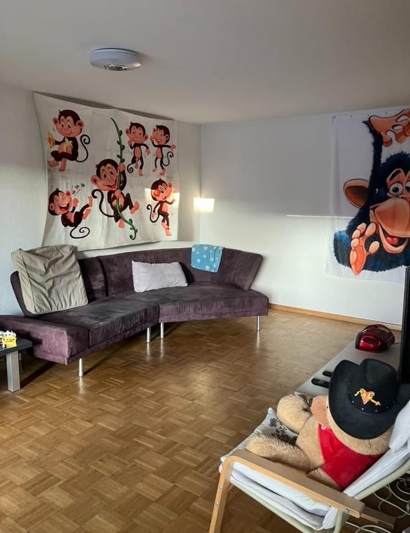 living room with a large sofa, wooden floor, monkey wall art, table with teddy bear