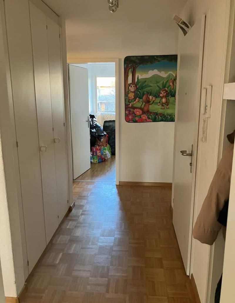 Empty corridor with wooden floors, white walls, and two white wardrobes on the left. Picture frame and a telephone on the right wall. Doors leading to another room.