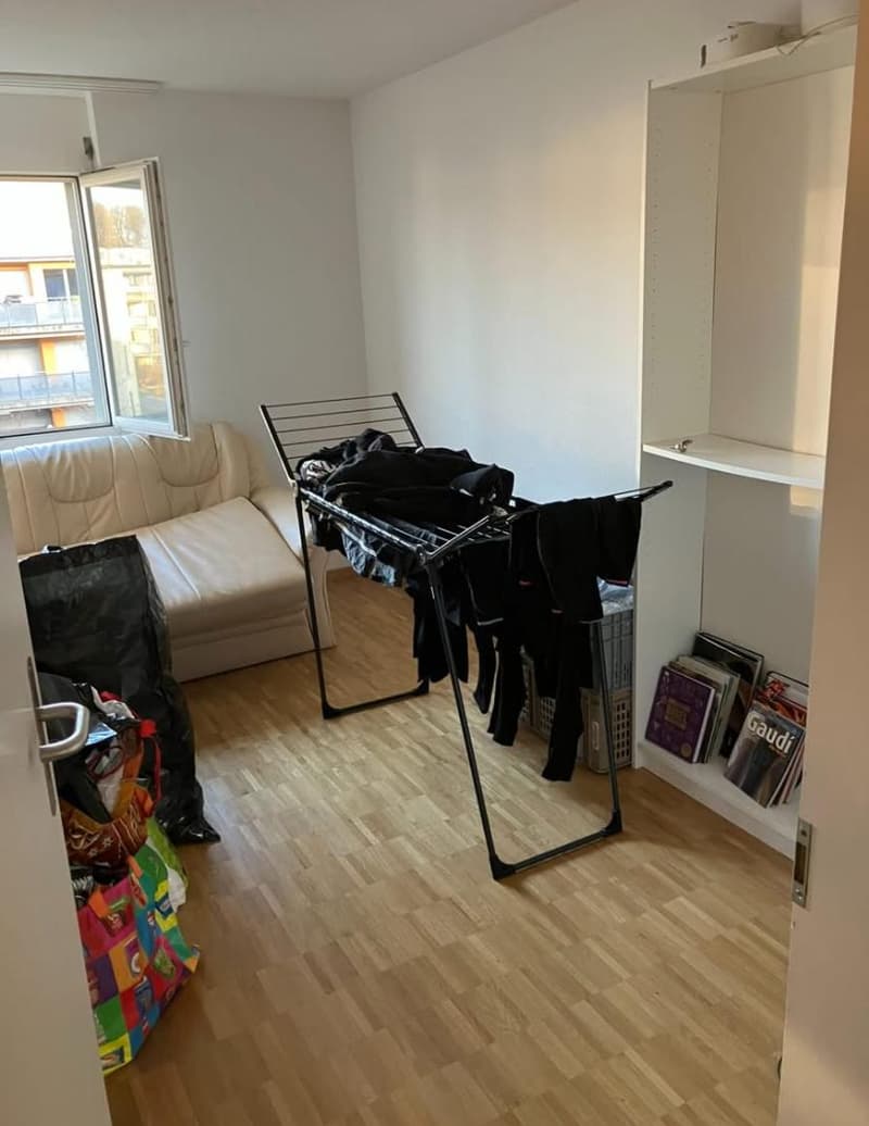 small room with wooden floor, a couch, storage boxes, a clothing rack, books on shelf