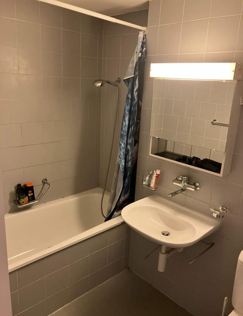 modern style bathroom with tile walls and floor, white bathtub, glass shelf for toiletries, modern faucet, mirror and bright light, toilet seat