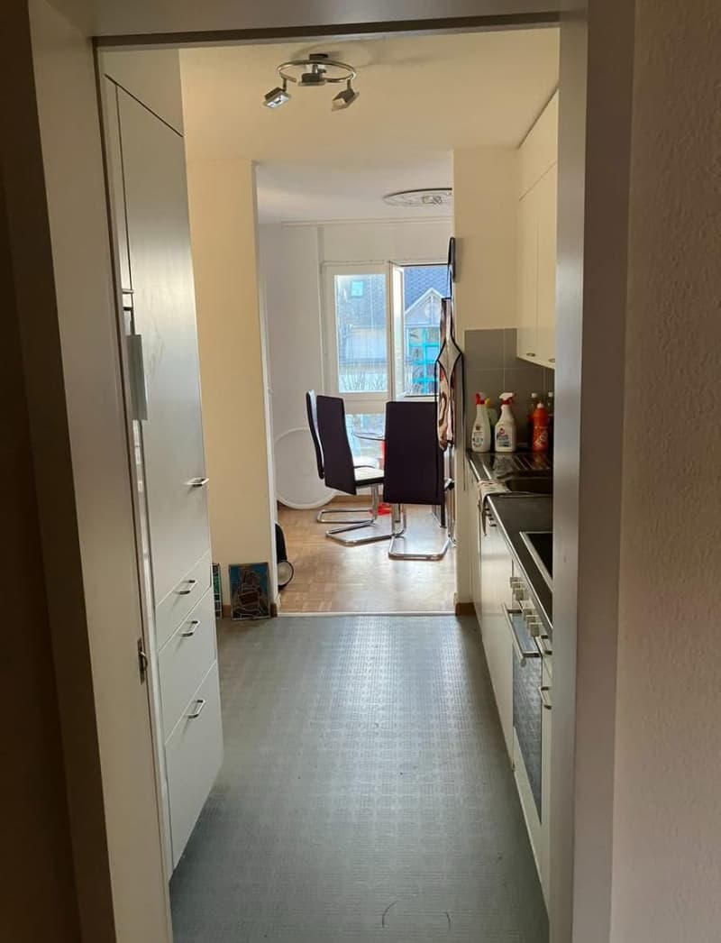 Empty hallway leading to kitchen with sink, chairs, and table visible in the distance