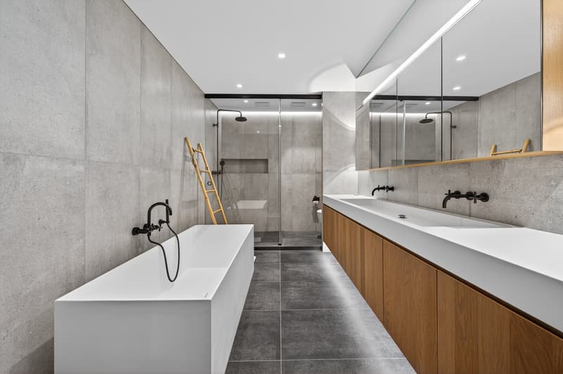 Bathtub, two sinks, large mirror, two showers, wooden cabinet, gray tiled floor