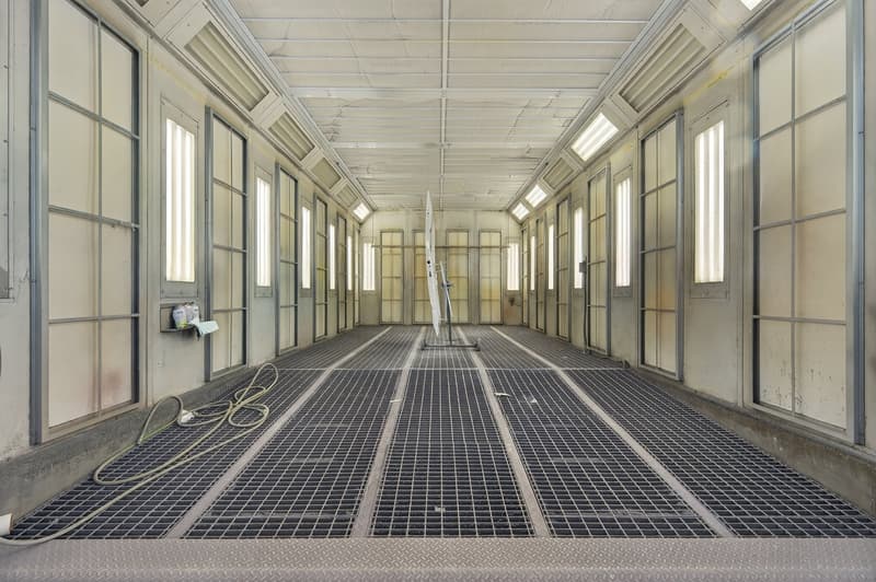 Empty corridor with high ceilings, metal grate flooring, large glass windows, metal walls, ceiling ventilation, a folded white stand in the center