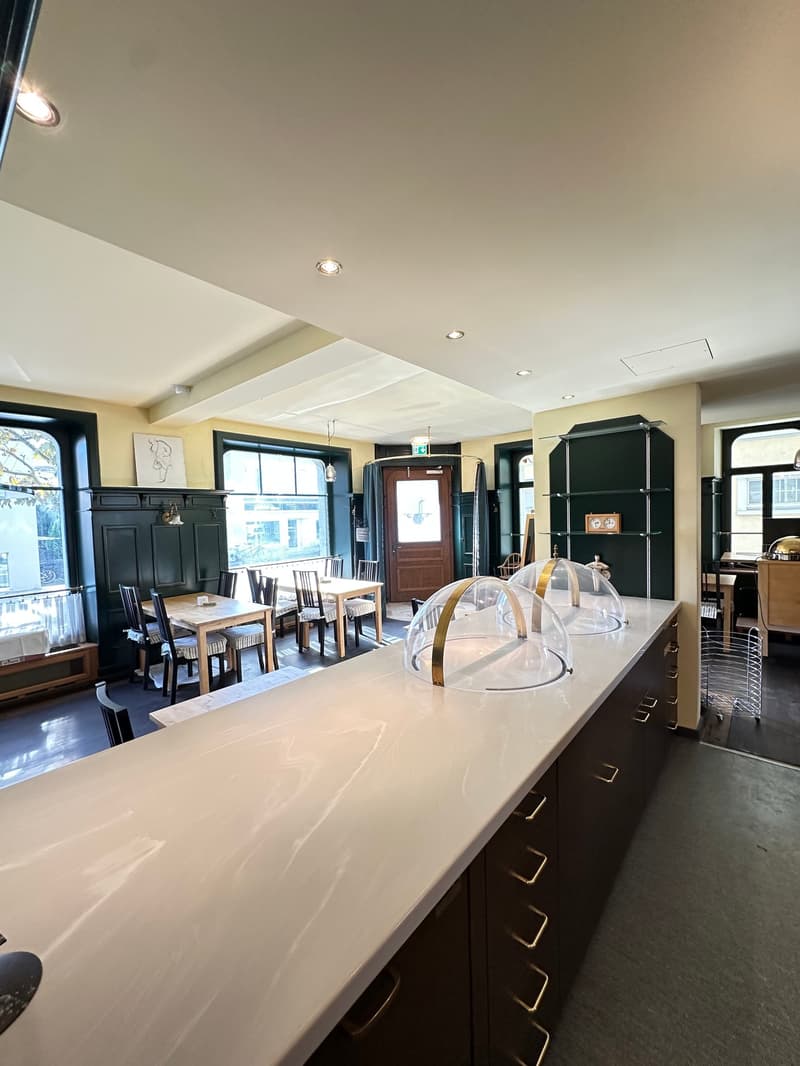 Dining room with large counter, tables, chairs, green wall, shelves, large windows