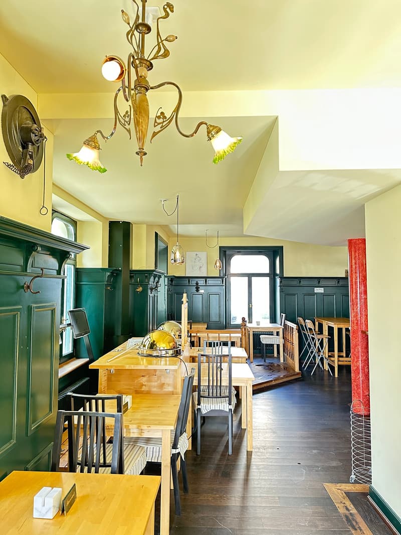 restaurant with wooden floors, chandelier, wooden chairs, green walls, tables, and windows