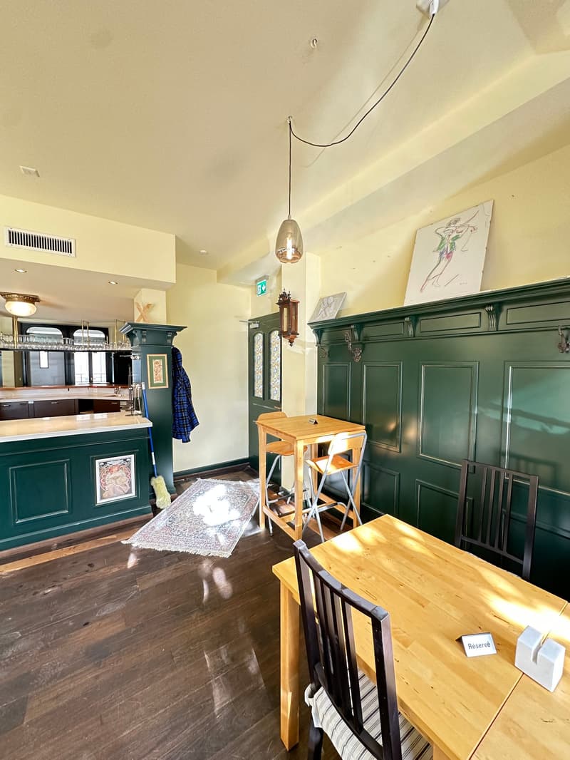 wooden tables and chairs, wooden flooring, dark green wainscoting, hanging pendant light, green counter, white ceiling