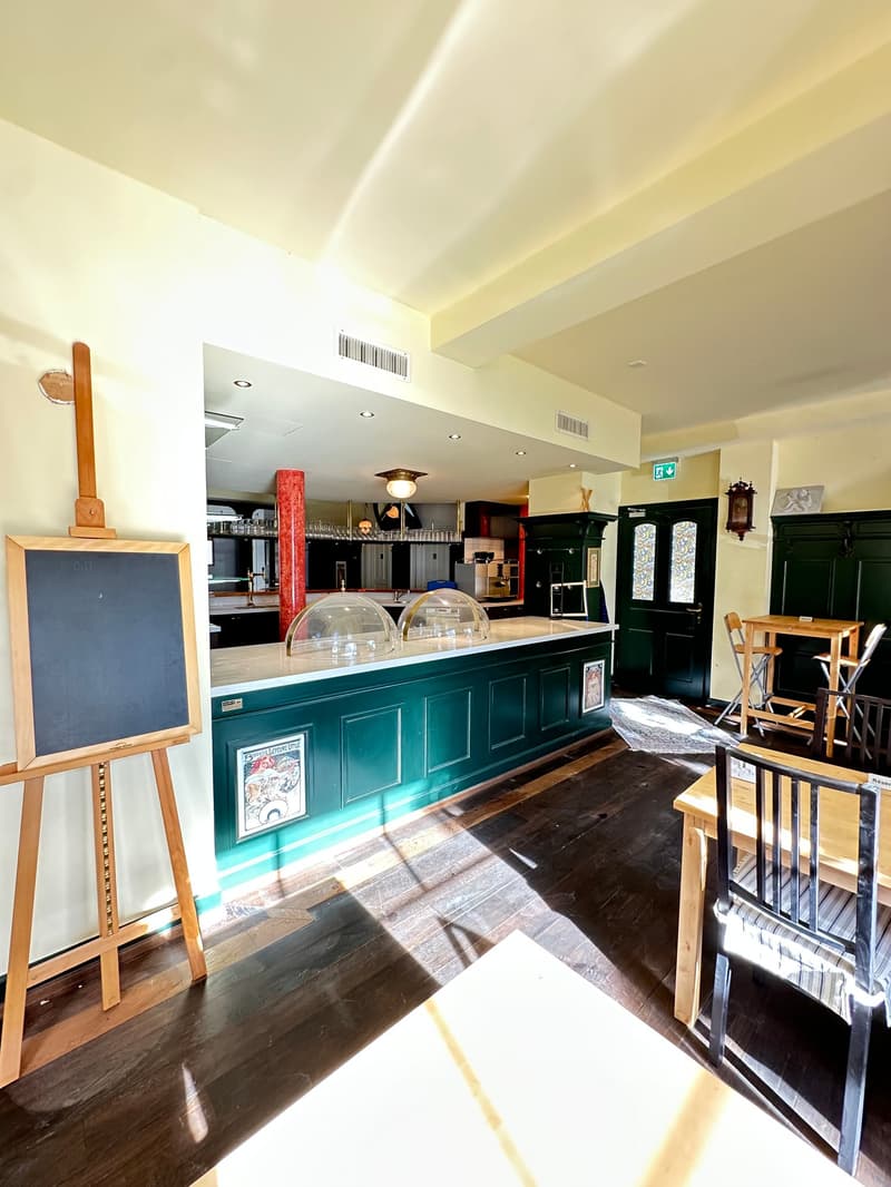 counter with food cabinets, blackboard, bar tables, chairs, open ceiling, lamps