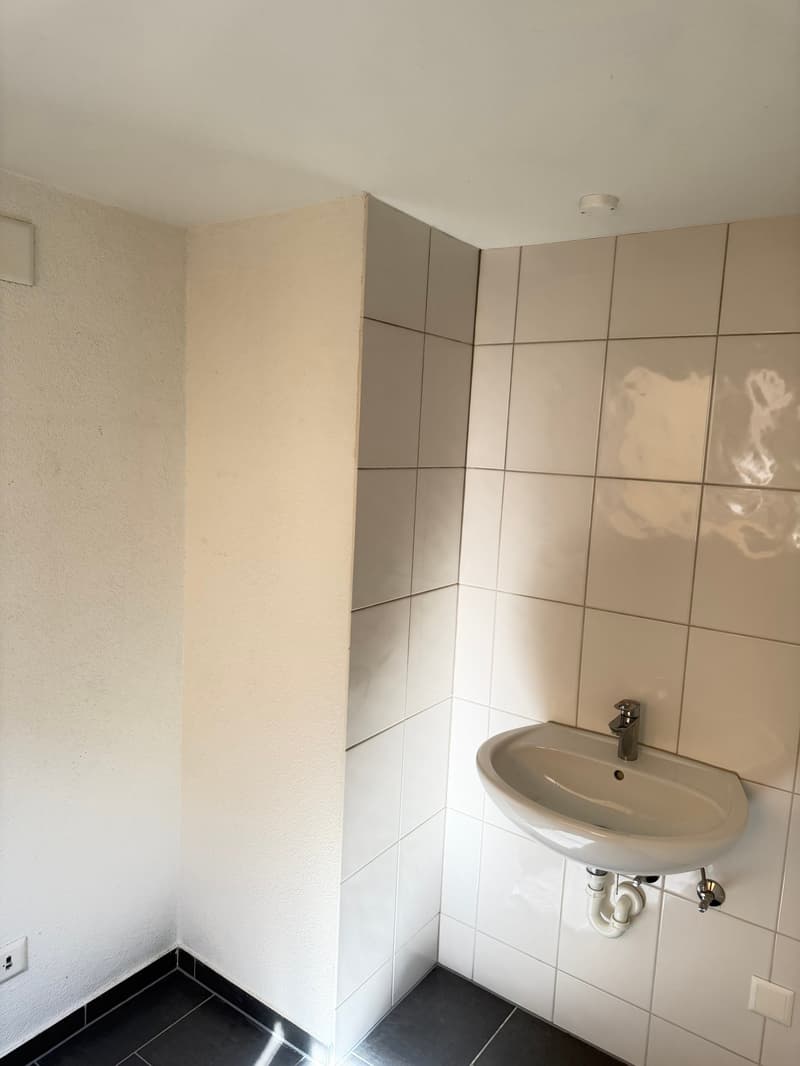 small room with white tiles, white sink, white walls, black floor