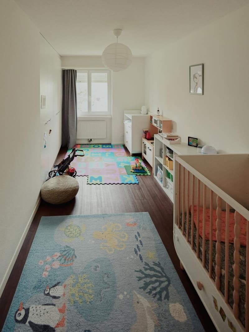 A nursery with crib, carpet, toys, shelves, cabinet, and light.