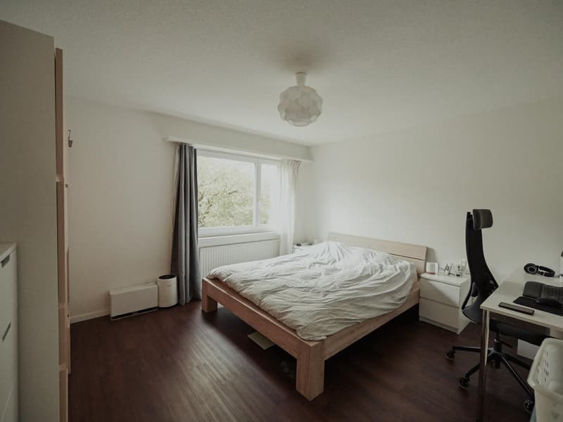 white walls, wooden bed, desk, chair, window with curtains, radiator