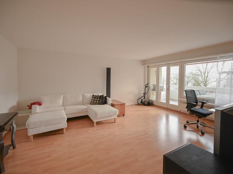 living room with wooden floor, white sofa, white walls, sliding doors to balcony, modern office chair, glass coffee table