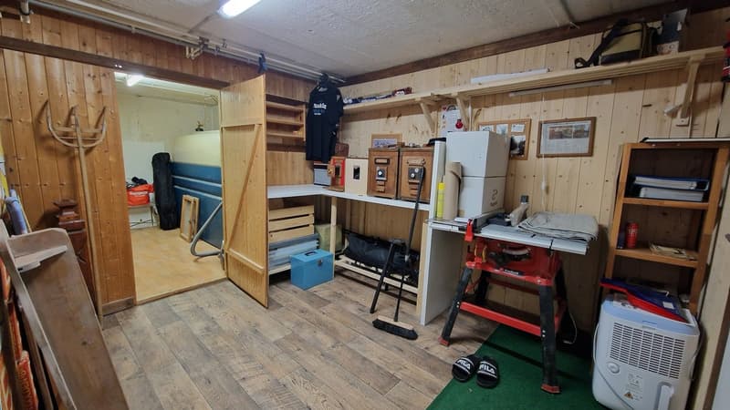 Workshop space with wooden walls, shelves, wooden flooring, storage boxes, cabinets, an open door, a workbench, and various tools and equipment.