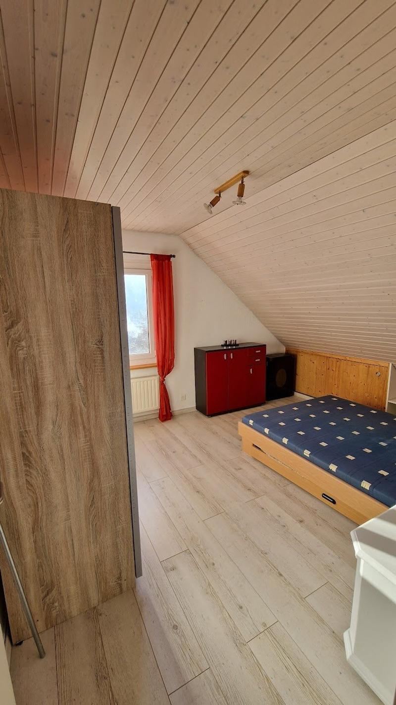 small room, wooden bed, blue bedding, wooden cabinet, red curtain, wooden ceiling, wooden floor