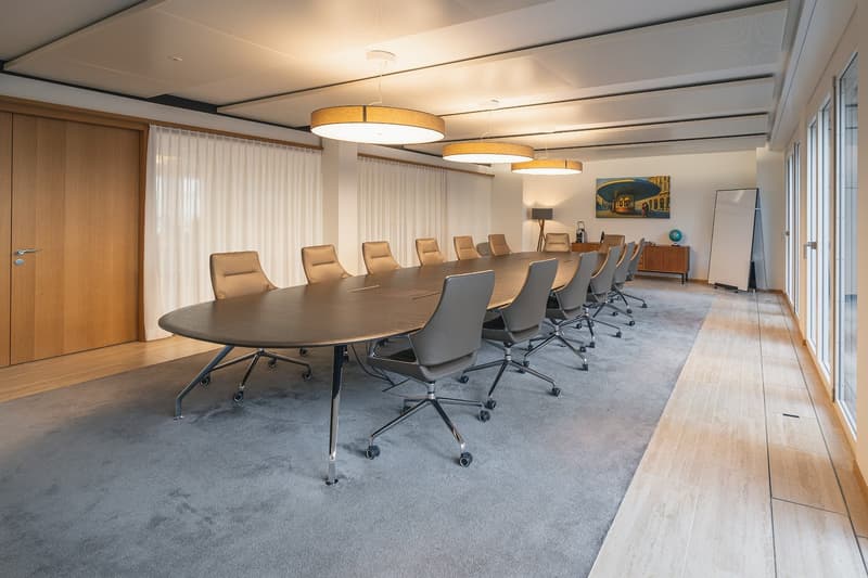 Long conference table, modern office chairs, three pendant lamps, wooden door, white drapes, artwork on wall, wooden floor