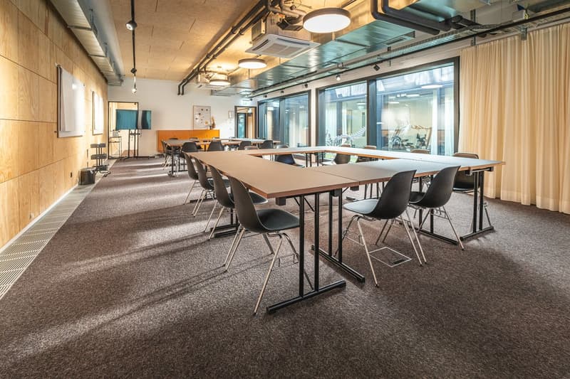 conference room with long wooden tables and black chairs, large windows, white walls, wooden floor, ceiling lights, whiteboards on the wall
