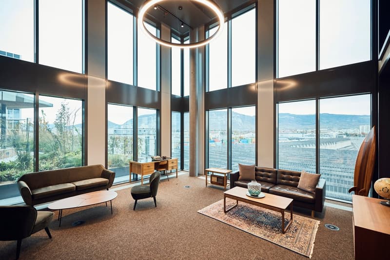 large windows, round chandelier, leather sofas, wooden coffee tables, desk, chair, rug