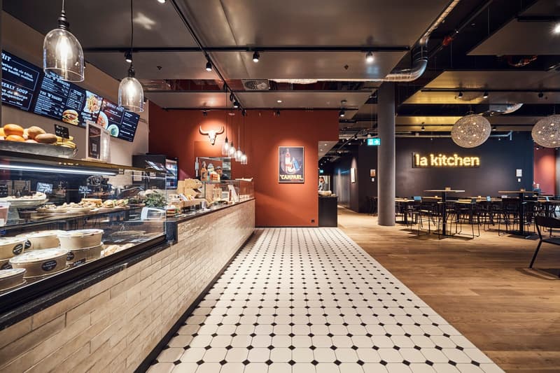 A restaurant with modern design features, a wooden floor, orange walls, wooden ceiling lights, and black-and-white patterned floor tiles.