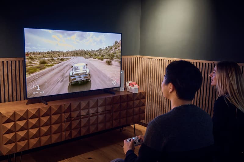 wooden entertainment center, black wall, two people playing game, large monitor