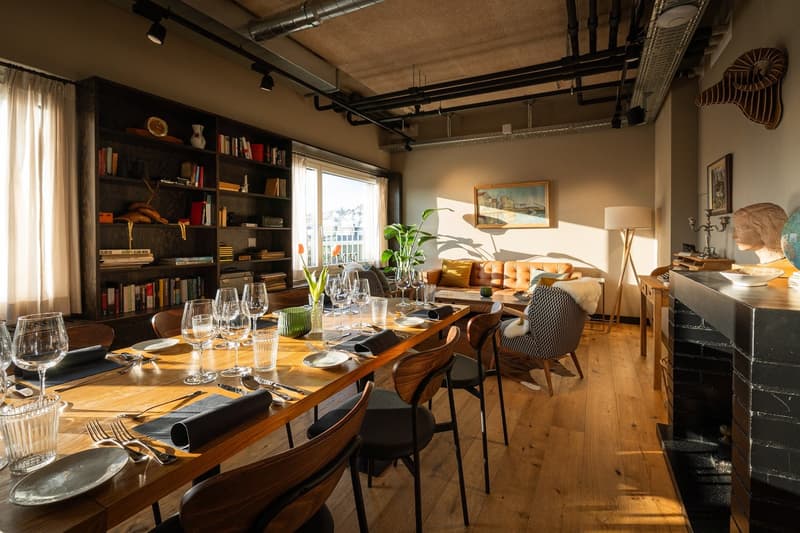long wooden table, wooden chairs, white plates, glasses, silverware, bookshelf, sofa, wooden floor, lamps, picture frames