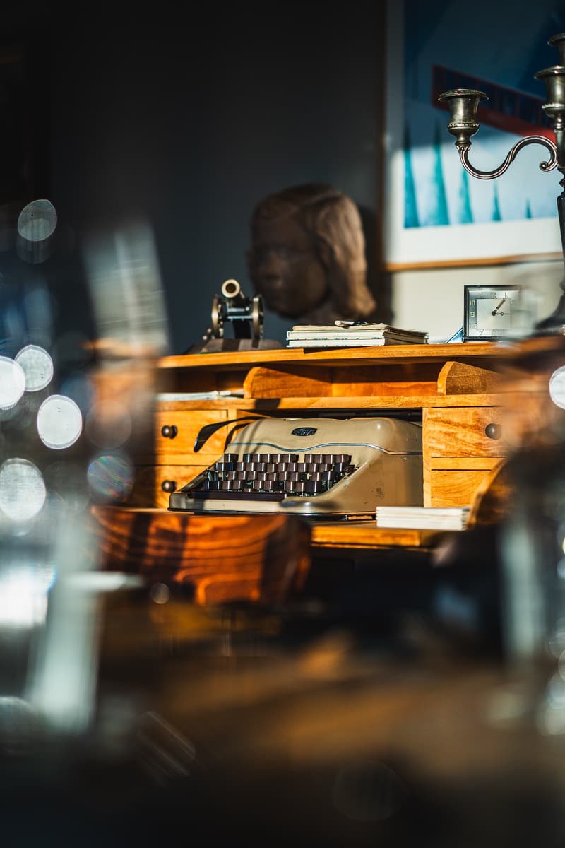 antique wooden desk with typewriter and clock, behind a bust of a woman