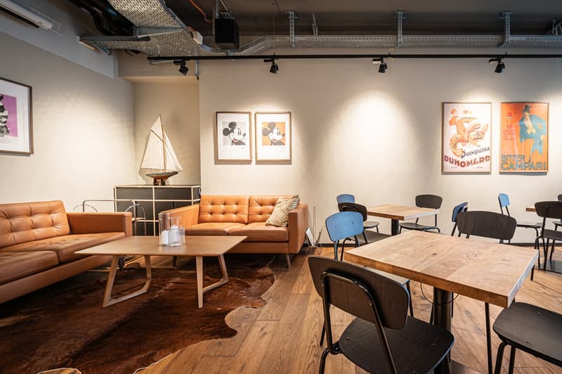 modern interior with wooden furniture, beige leather sofa, white and blue chairs, wooden tables, light fixtures, posters on the wall, wooden flooring