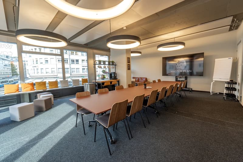 Empty meeting room with long wooden table, chairs, couch, TV, windows, ceiling lamps