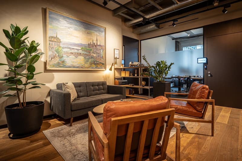 modern living room with gray sofa, brown wooden chairs, rug, plant, wooden floor, painting, and coffee table