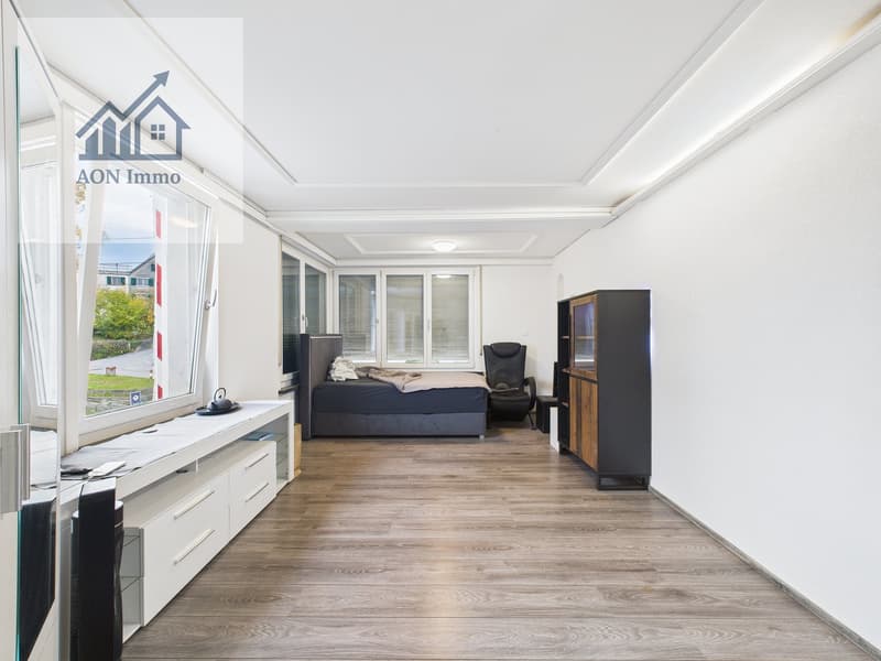 Empty room with wooden floor, white walls, large window, bed, chair, cabinet, desk