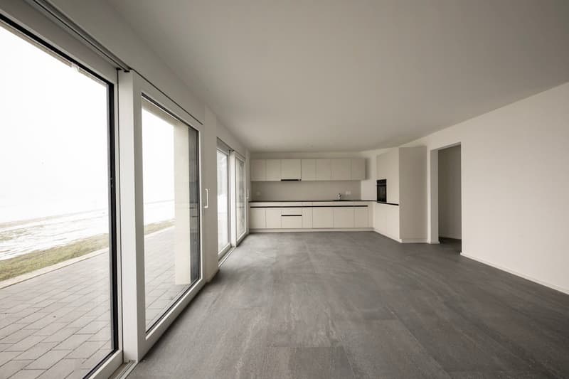 white walls, gray flooring, kitchen area with cabinets, countertops, sink, open sliding glass doors to balcony